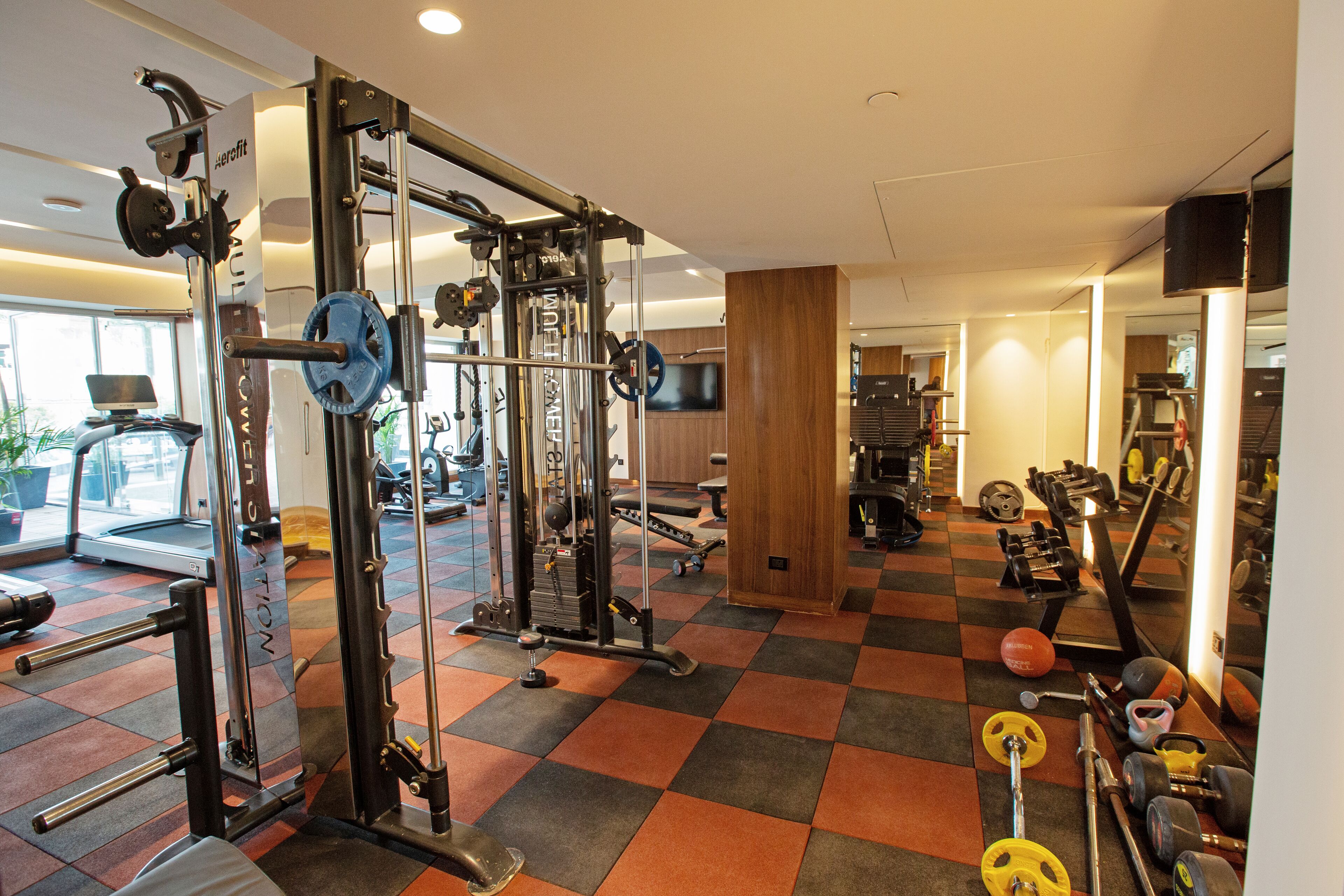 A gym with various exercise equipment, a checkered floor, and a television on the wall.