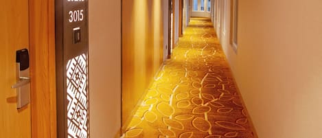 Un pasillo de hotel con alfombra estampada, una puerta de madera y un diseño geométrico en la pared.