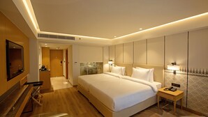 A modern hotel room with a large bed, a desk, a TV, and a bathroom visible through a glass partition. - ARISTA BY AMBITION (Guwahati)