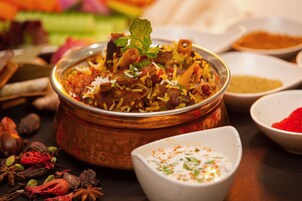 Un plato de biryani con un cuenco de cobre, rodeado de especias y un tazón pequeño de raita.