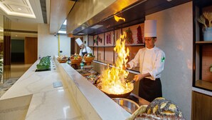 A chef cooking with flames in a modern kitchen with marble countertops and a long serving counter. - ARISTA BY AMBITION (Guwahati)