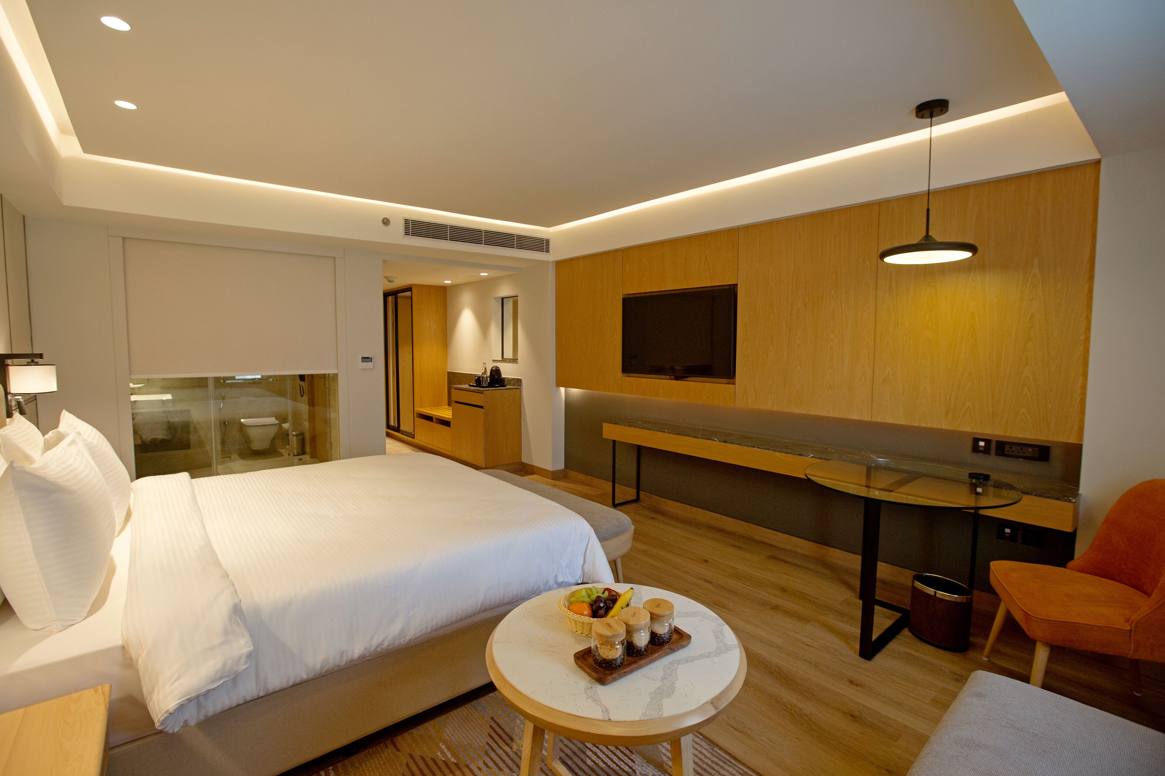 A modern hotel room with a large bed, a small round table with snacks, a seating area, and a TV mounted on the wall.