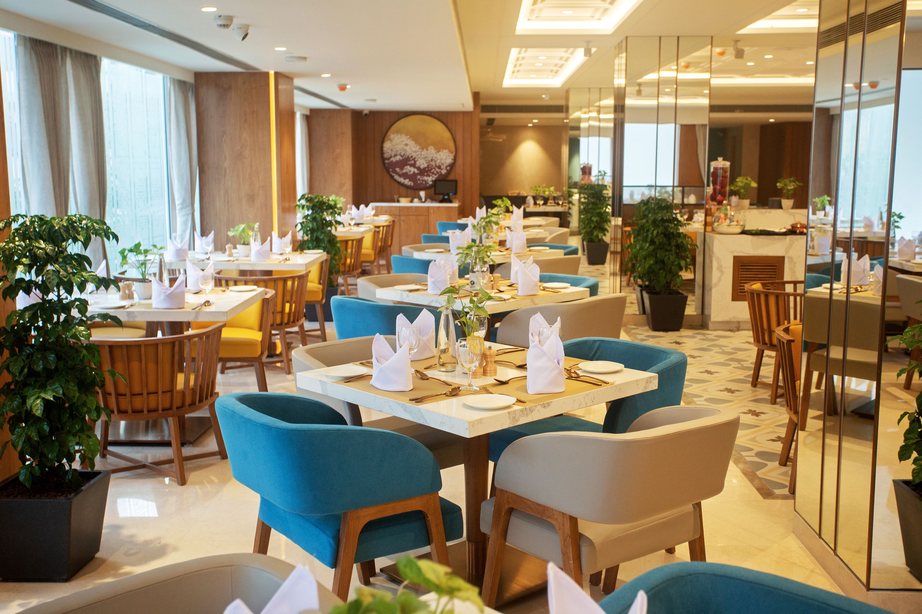 A modern restaurant with blue and wooden chairs, white table settings, and potted plants.