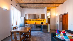A modern kitchen with stainless steel appliances, a dining area with a wooden table and chairs, and a black sofa with colorful cushions. - Casa Bodoni in Rome With 2 Bedrooms and 2 Bathrooms (Rome)