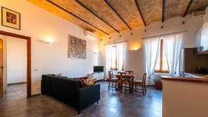 A living room with a sofa, a dining table with chairs, a kitchen area, and a ceiling with exposed beams. - Casa Bodoni in Rome With 2 Bedrooms and 2 Bathrooms (Rome)