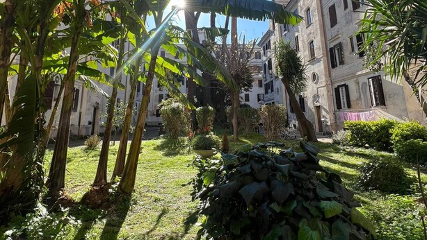 A courtyard with a stone wall, palm trees, and a building with multiple windows and balconies. - Casa Bodoni in Rome With 2 Bedrooms and 2 Bathrooms (Rome)