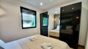 Ein modernes Hotelzimmer mit einem großen Bett, einem Fenster mit Blick auf ein traditionelles Gebäude und einem separaten Schlafbereich mit Bett und Nachttisch.