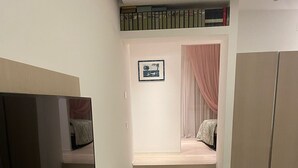 A modern, minimalist room with a large flat-screen TV, a staircase leading to a bedroom with a bed and a window, and a bookshelf with books. - A DUE PASSI (Piattoni-Villa Sant'Antonio)
