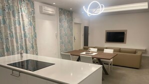A modern kitchen with a central island, a dining area with a wooden table and chairs, and a beige sofa in a living area. - A DUE PASSI (Piattoni-Villa Sant'Antonio)