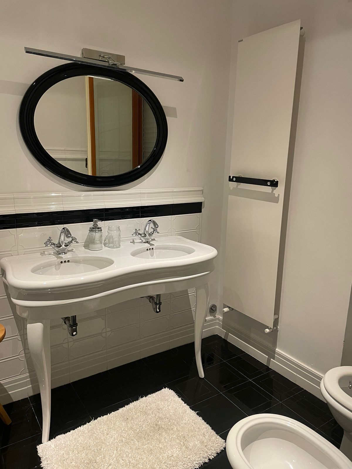 A bathroom with a white sink, two faucets, a mirror, a toilet, and a white rug.