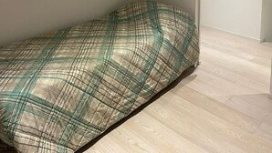 A small, single-bed room with a plain white wall, a wooden floor, and a closed door. - A DUE PASSI (Piattoni-Villa Sant'Antonio)