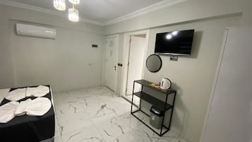 A hotel room with a bed, a TV, a mirror, and a small table with a kettle.