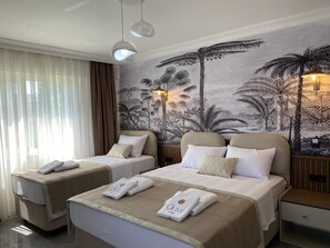 Quarto de hotel com duas camas, um grande mural de árvores tropicais e uma janela com cortinas leves.