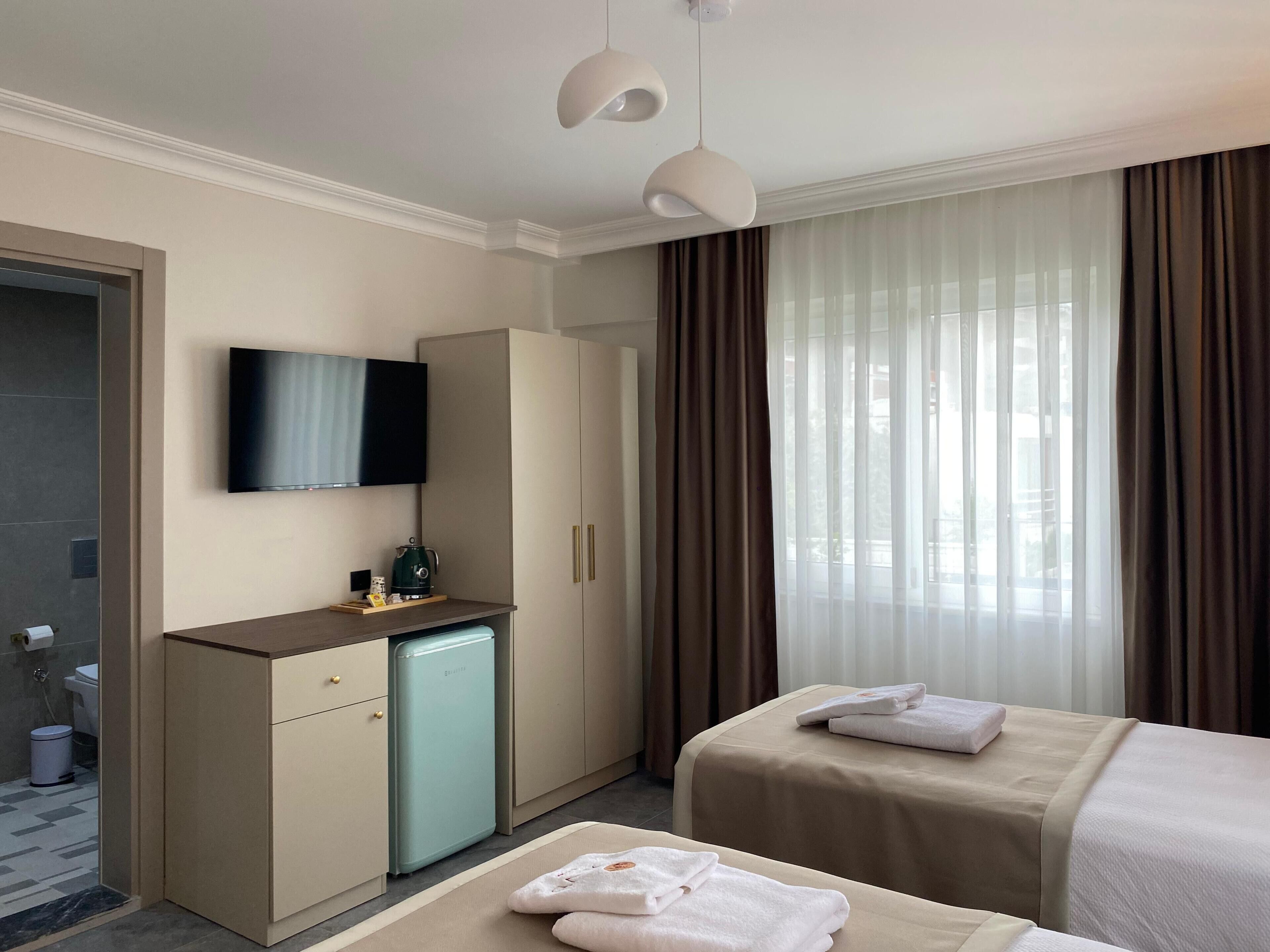 A hotel room with a bed, a TV, a minibar, a shower area, and a window with curtains.