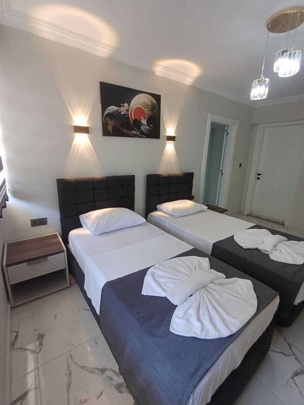 Quarto de hotel com duas camas, uma mesinha de cabeceira, um quadro e duas luminárias de parede.