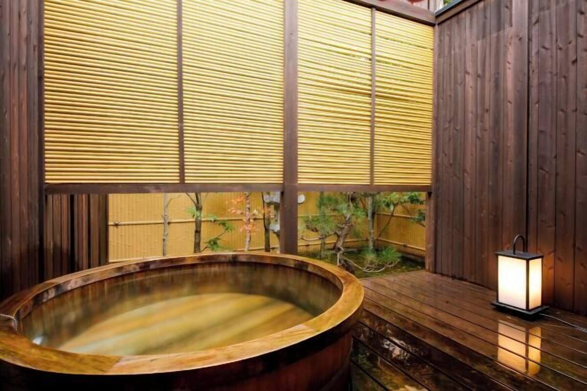 A wooden hot tub with a bamboo screen backdrop, a wooden deck, and a lantern.