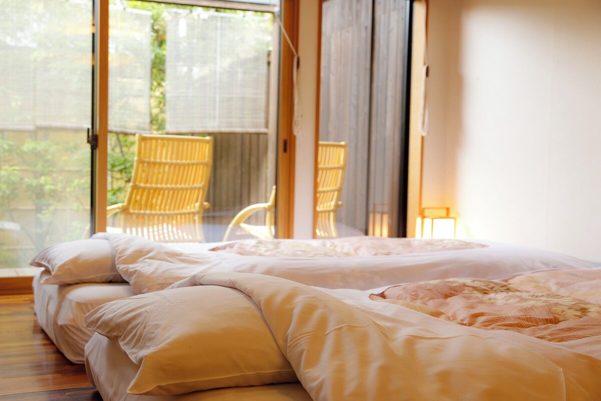 A bedroom with a large sliding glass door leading to a balcony, a bed with white bedding, and a wicker chair.