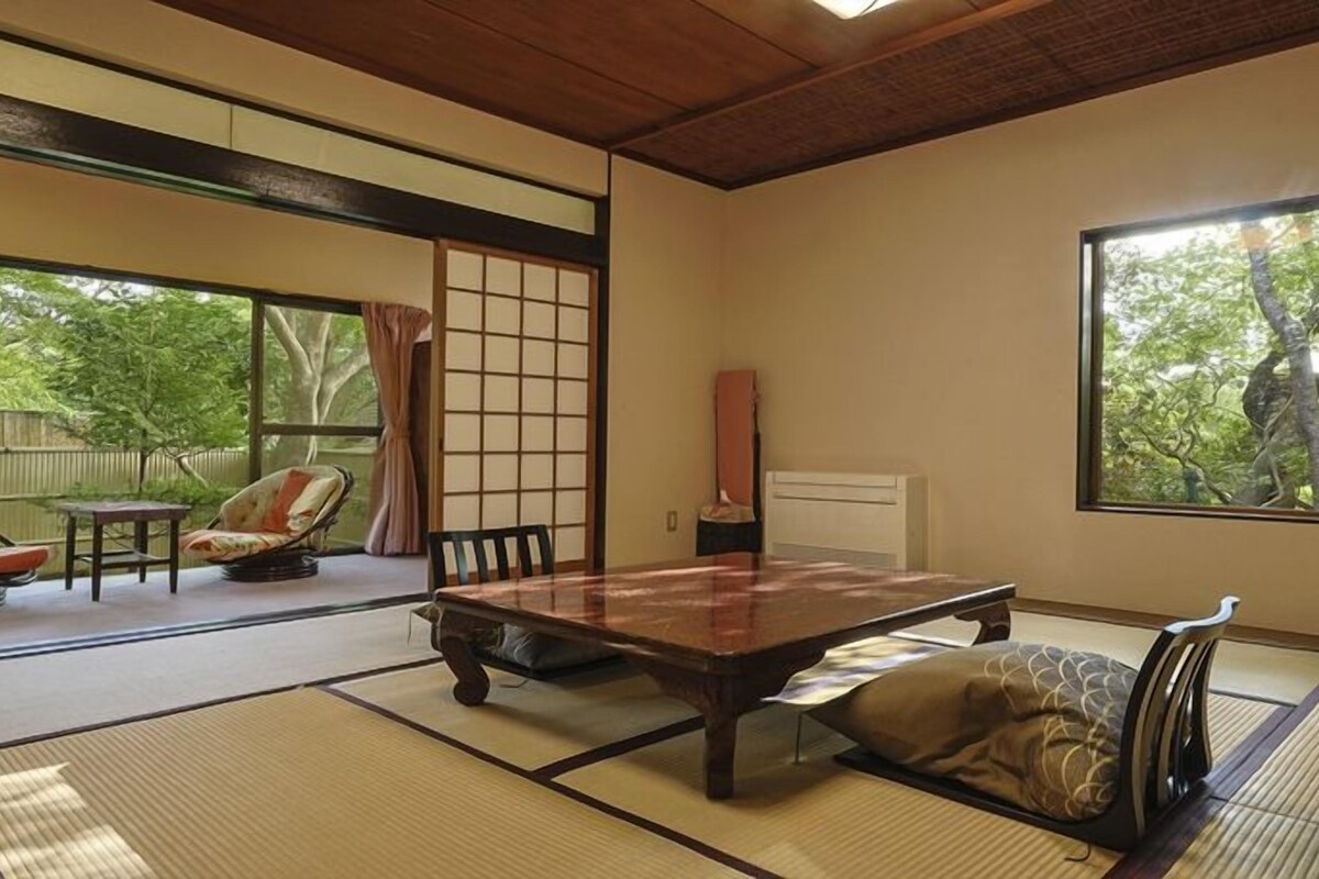 A traditional Japanese room with tatami flooring, a low table, and a sliding door leading to an outdoor area.