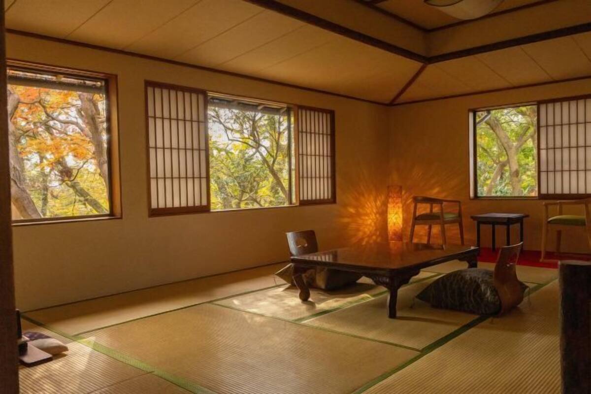 A tatami mat room with a low table, chairs, and a traditional Japanese-style window with a view of trees.