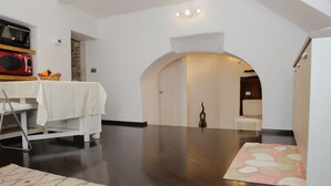 A spacious room with a dark wooden floor, a white dining table with a tablecloth, a microwave, and a fruit basket. - La Petite Maison (Ruvo di Puglia)