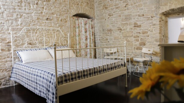 A room with a metal bed, white curtains, and a stone wall. - La Petite Maison (Ruvo di Puglia)