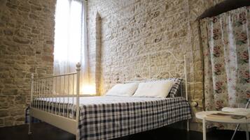 A bedroom with a stone wall, a bed with a checkered bedspread, and a window with curtains.