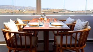 Een houten eettafel met vier stoelen, gedekt met borden, glazen en een zout- en peperstel. De tafel staat bij een groot raam met uitzicht op een verafgelegen landschap.