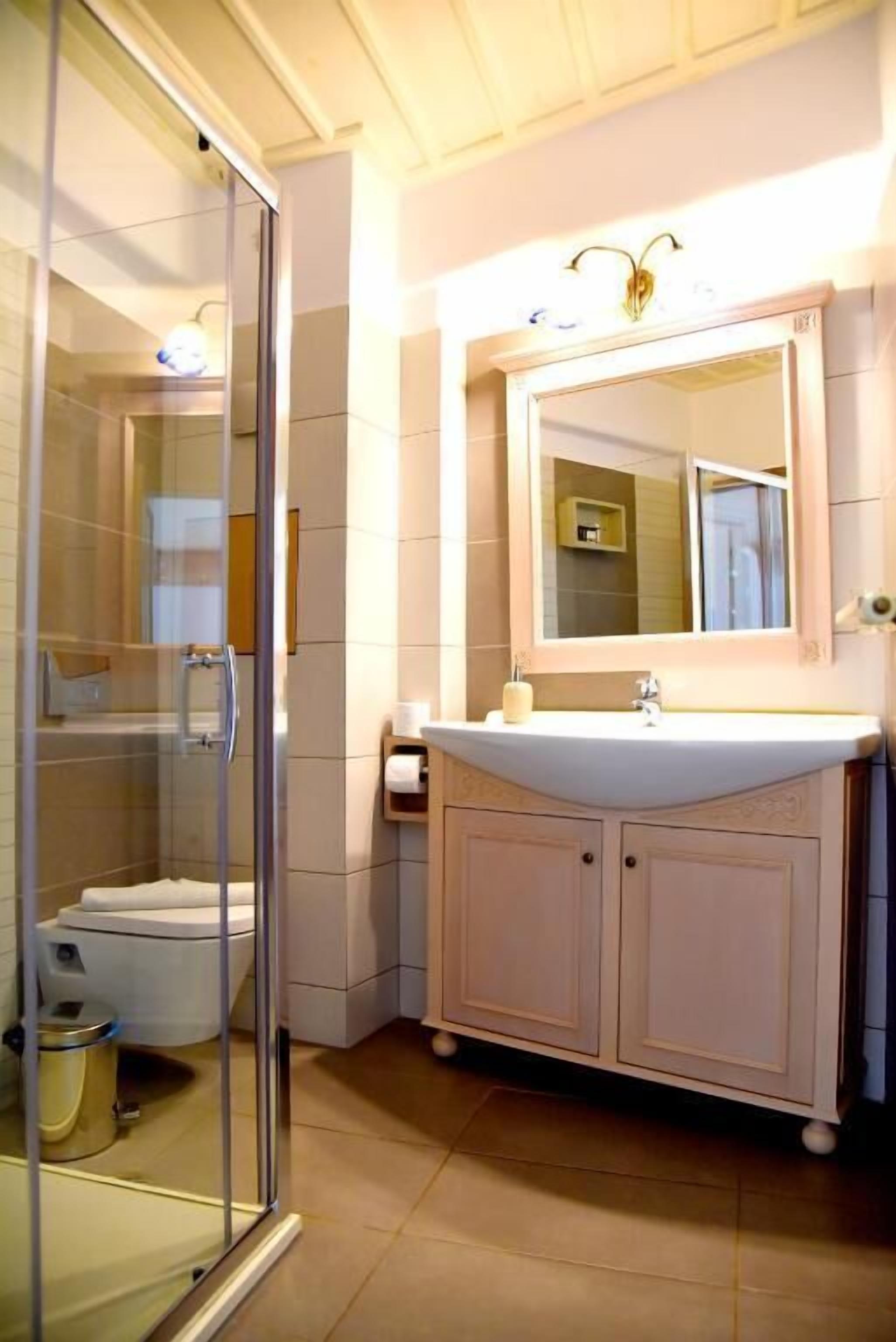A bathroom with a glass shower enclosure, a white sink with a mirror above it, and a toilet.
