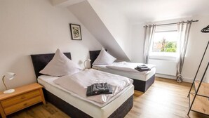 Een slaapkamer met twee bedden, een nachtkastje, een lamp en een raam met gordijnen.