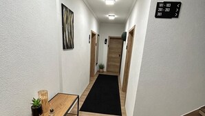 Een hal met een houten tafel, een zwart vloerkleed en een bord waarop de kamer nummers 101-103, 201-203 en 301 staan.