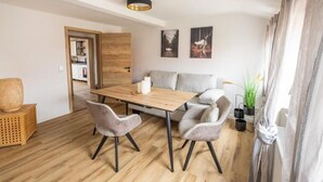 Een moderne woonkamer met een houten eettafel, grijs gestoffeerde stoelen, een grijze bank en een houten accentmuur.