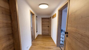 Een gang met houten vloeren en deuren, die uitkomt in een kamer met een bed en nachtkastje.