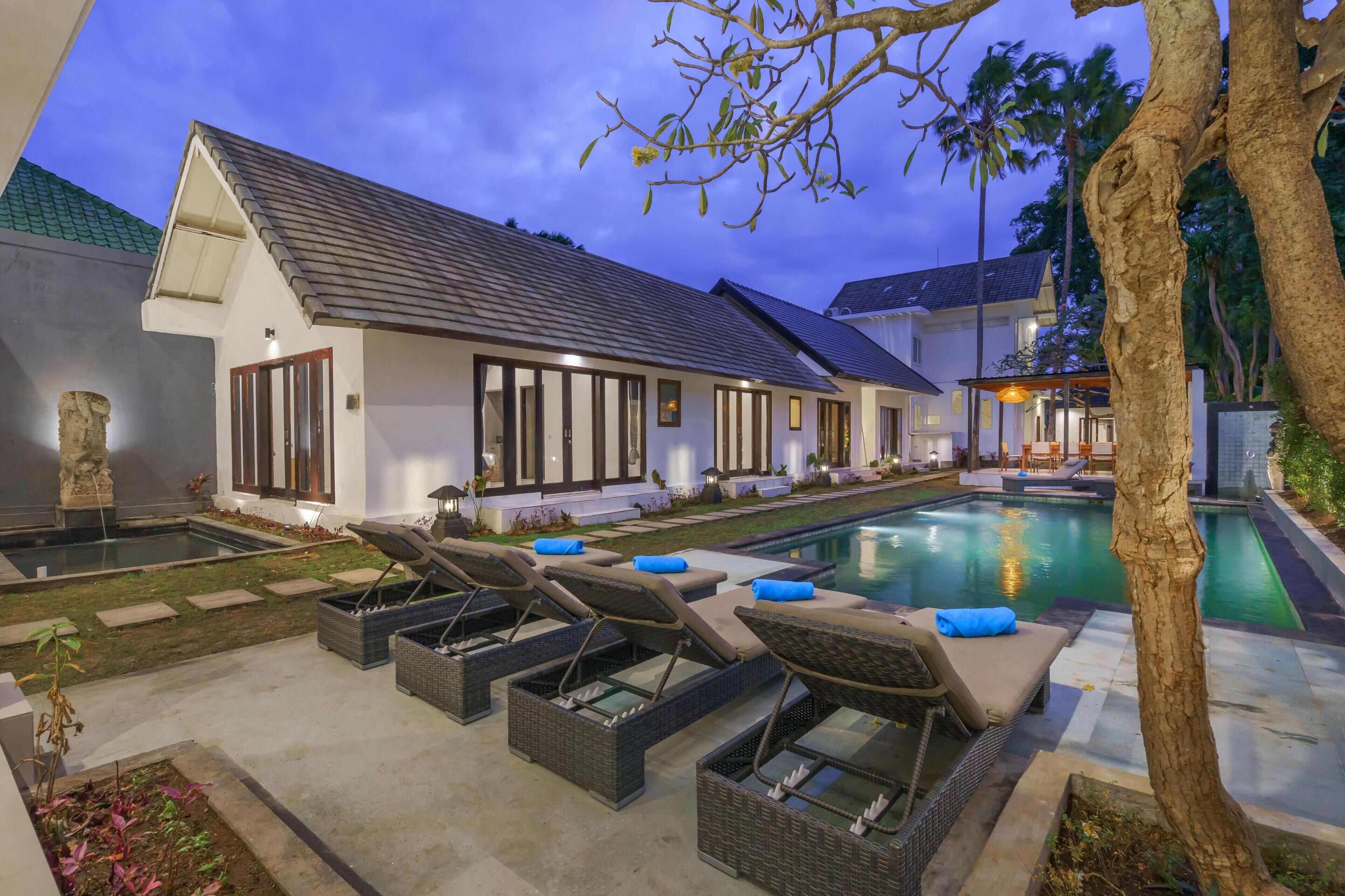Una villa moderna con piscina, sillas de descanso y un jardín bien cuidado.