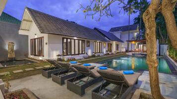 Una villa moderna con piscina, sillas de descanso y un jardín bien cuidado.