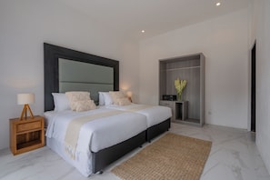 A modern bedroom with a large bed, bedside tables, a wardrobe, and a small desk with a lamp.