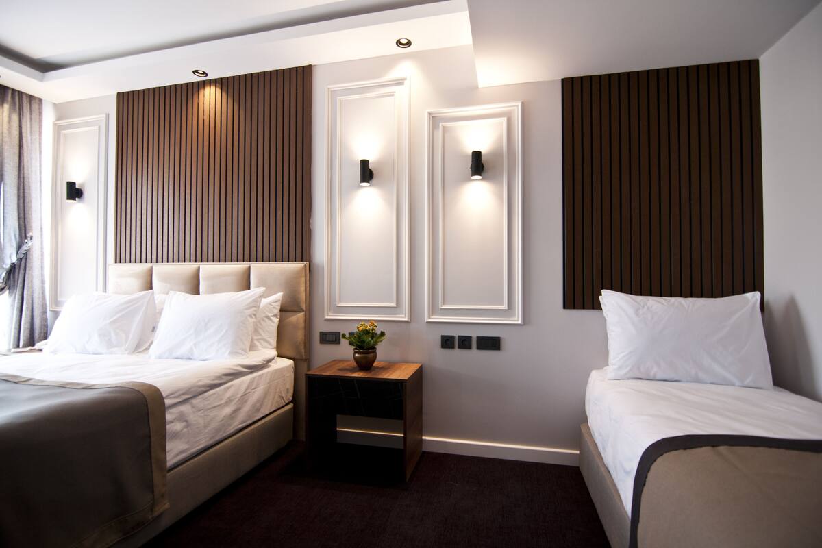 A modern hotel room with a large bed, a smaller bed, and a nightstand with a plant.