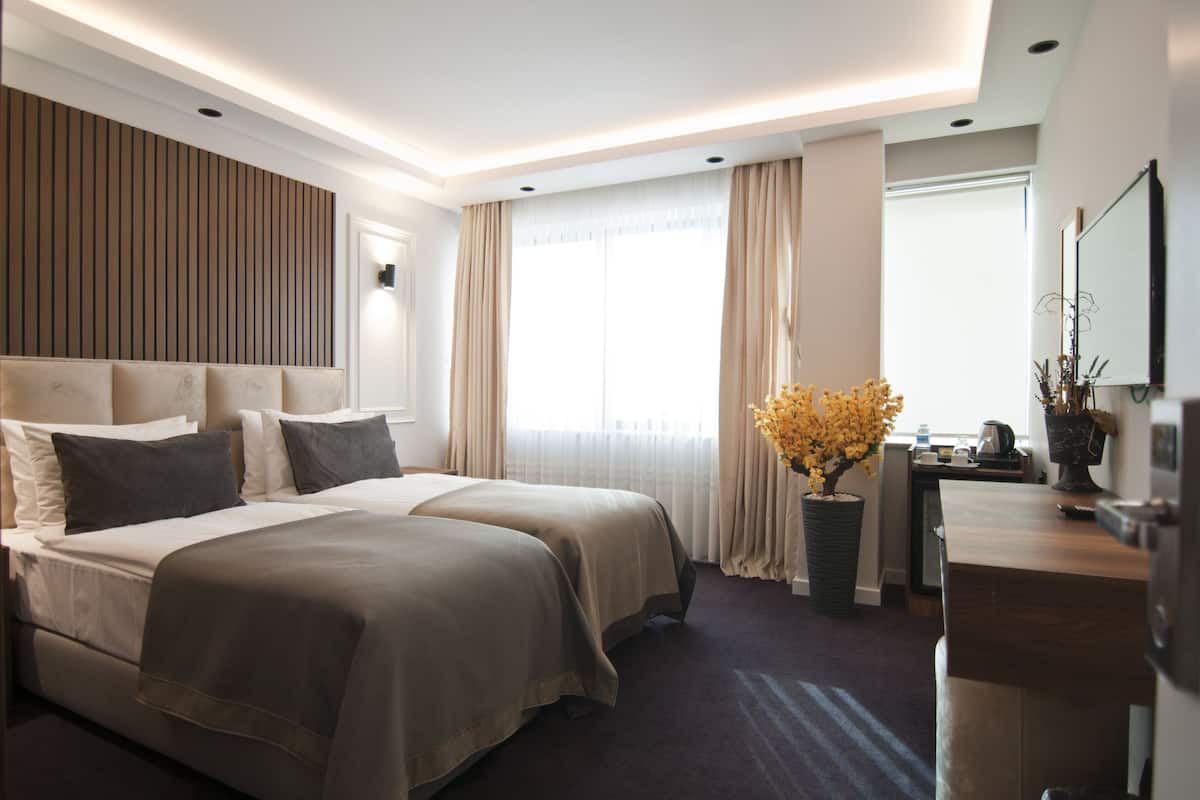 A hotel room with a large bed, a desk, a potted plant, and a window with curtains.