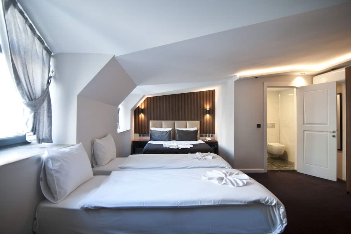 A hotel room with two beds, a wooden headboard, a nightstand, and a bathroom visible through an open door.