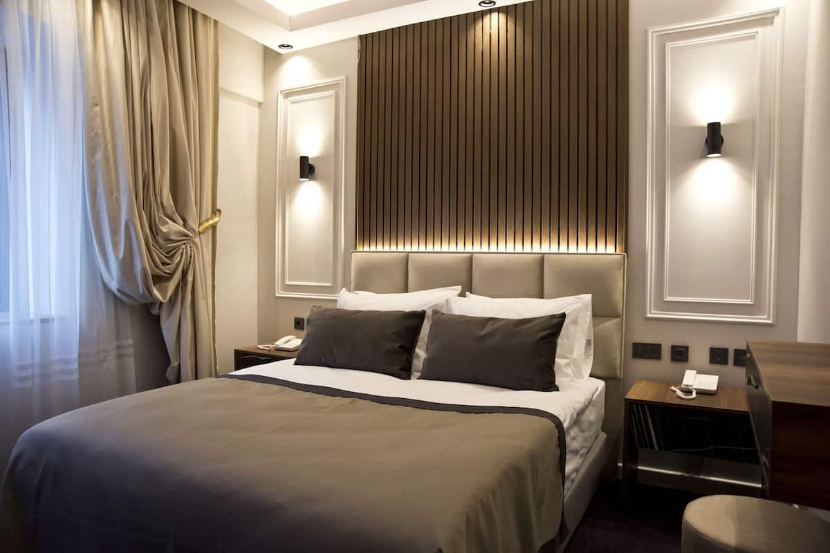A modern hotel room with a large bed, a bedside table with a lamp, and a wall-mounted light fixture.
