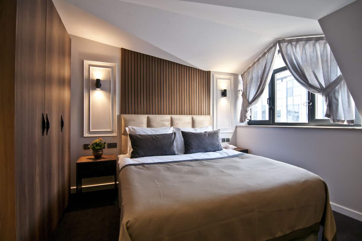 A hotel room with a large bed, bedside tables, a wall-mounted light, and a window with curtains.