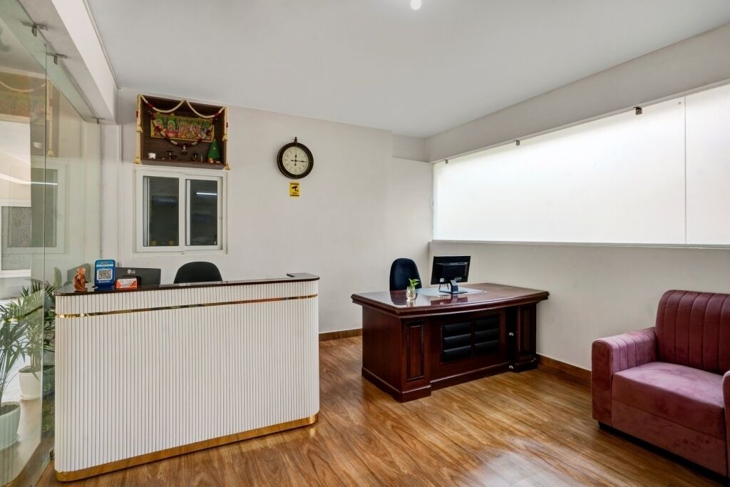 A reception area with a reception desk, a clock, a computer monitor, and a couch.