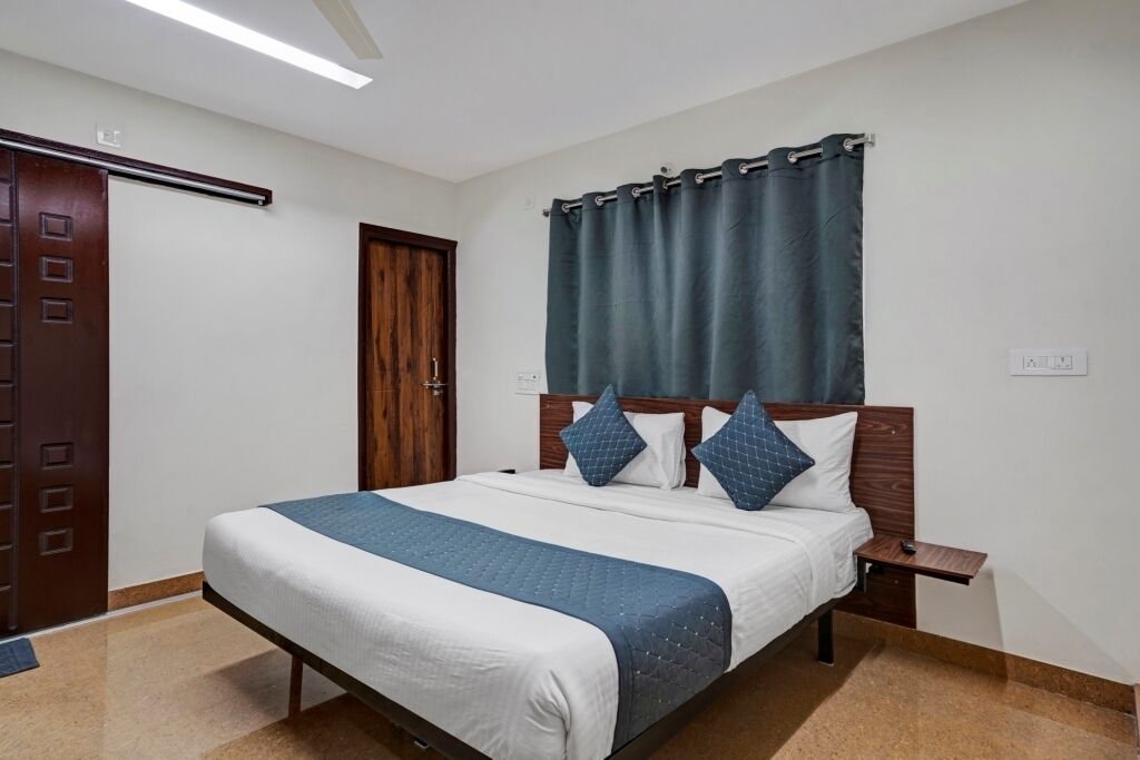 A hotel room with a bed, a nightstand, a wooden door, and a curtain.