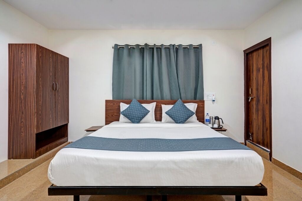 A standard hotel room with a bed, wooden wardrobe, and a window with curtains.