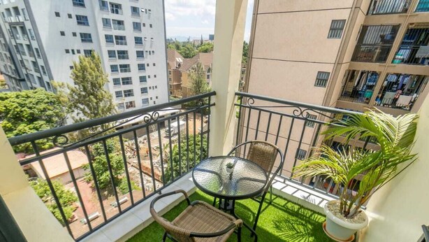 Ein Balkon mit einem kleinen Tisch und Stühlen, einem Blumentopf und Blick auf die umliegenden Gebäude.