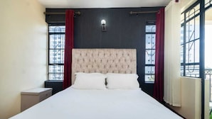 Ein Schlafzimmer mit einem großen Bett, zwei Nachttischen, einer Wandleuchte und einem Fenster mit Blick auf Gebäude.
