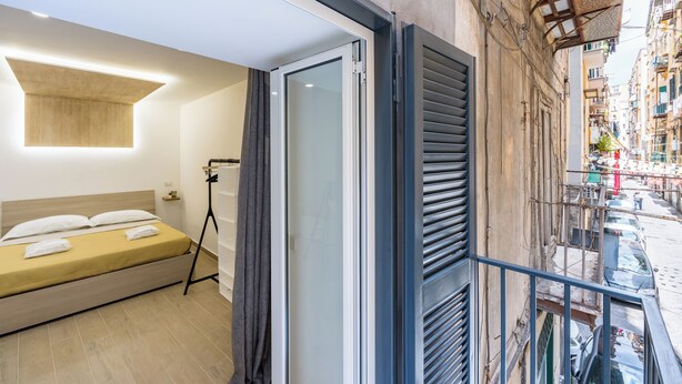 A modern hotel room with a bed, a balcony, and a view of the street. - Casa Fernanda (Naples)
