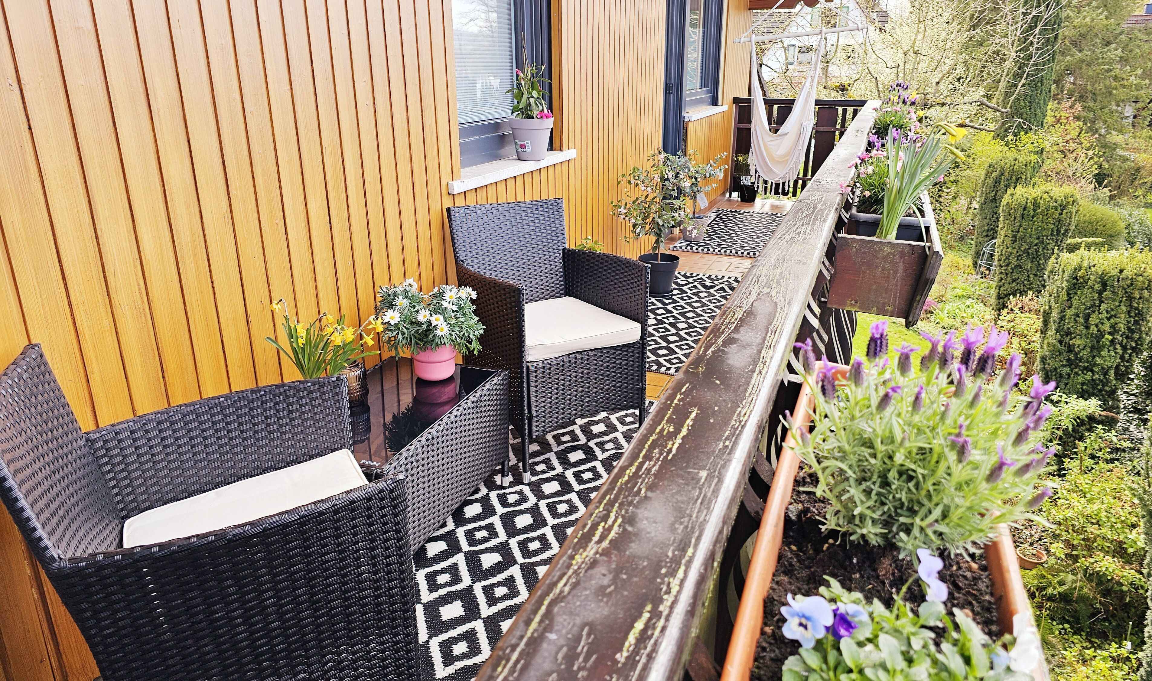 A balcony with wicker furniture, potted plants, and a wooden railing.