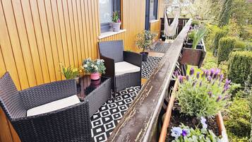 A balcony with wicker furniture, potted plants, and a wooden railing.