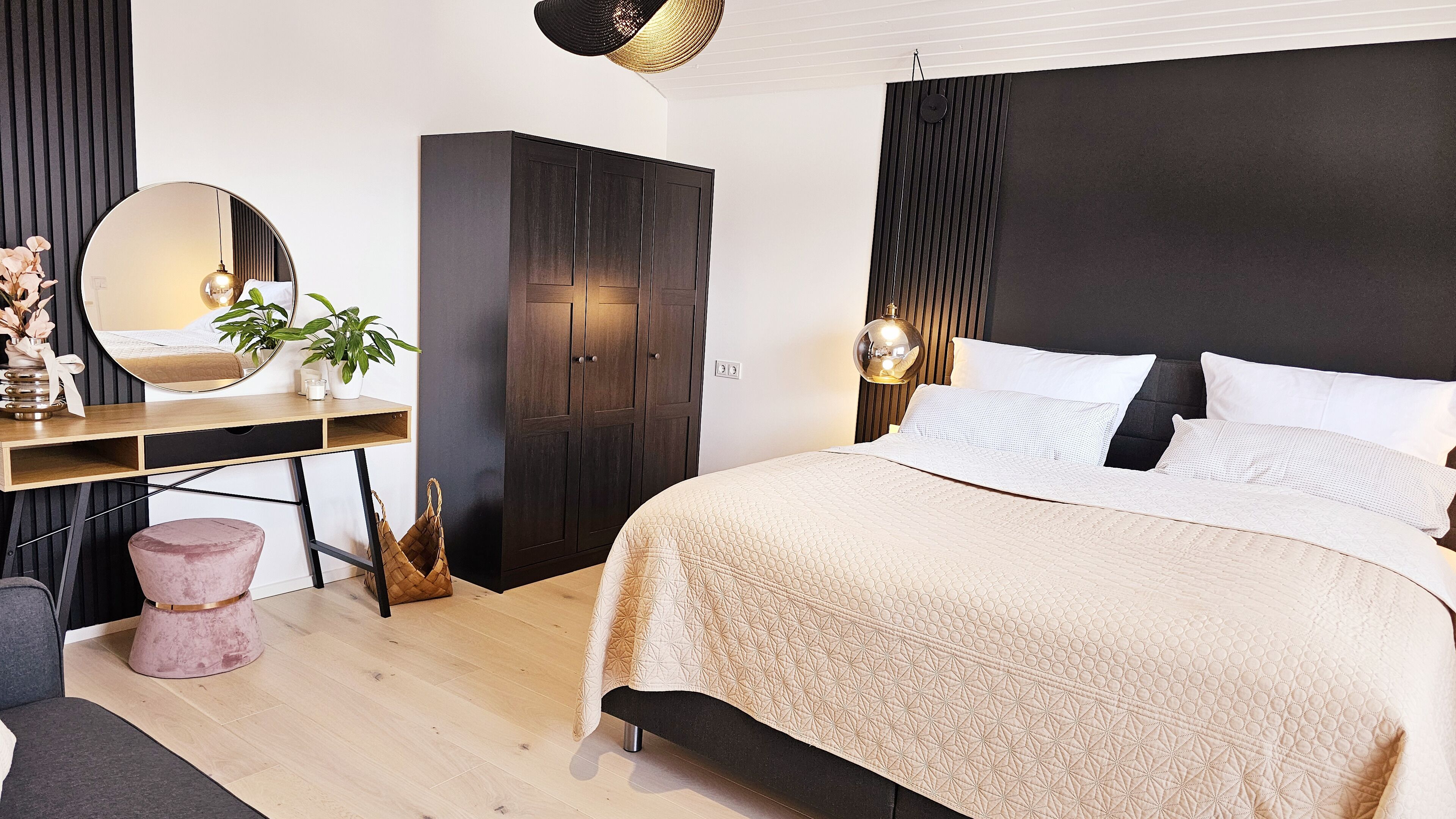 A modern bedroom with a large bed, a wooden desk, a wardrobe, and a round mirror.