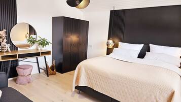 A modern bedroom with a large bed, a wooden desk, a wardrobe, and a round mirror.